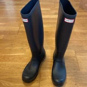 Hunter ORIGINALGummistövlar för dam - Hunter gummistövel i naturligt gummi Med högt skaft, rundad tå, logotyp upptill och dragflärp baktill. Med Hunter gummistövlar   får du inte bara ett praktiskt och vattentätt skydd,  du får ett riktigt fashion statement! Dessa stövlar kombinerar en modern, feminin look med hög funktionalitet och komforti.  Har använts endast några gånger..