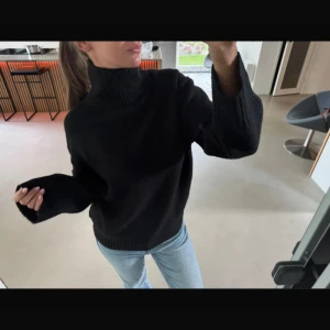 Svart polotröja  - Säljer en svart polotröja i stickat material med bred ribbad krage och muddar. Tröjan har en loose fit och långa ärmar, perfekt för kyliga dagar. Enkel och stilren design som är lätt att matcha med jeans eller kjol.