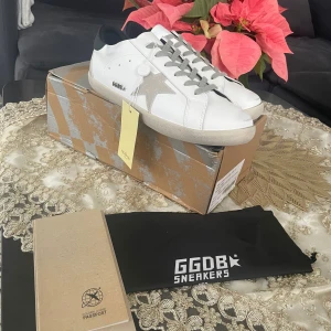 Golden goose - Golden Goose sneakers i vitt skinn med grå mockadetaljer och ikonisk stjärna på sidan. Skorna har grå snörning, svart hälparti och platt sula. Snygg och stilren design som passar perfekt till streetwear. Levereras med originalkartong och dustbag.