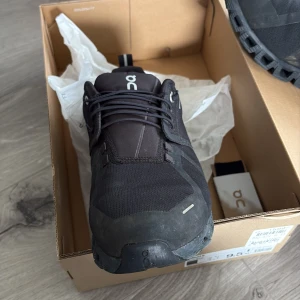 Svarta On Running sneakers EU 42.5 - Säljer ett par svarta On Running sneakers i storlek 42.5. Skorna har en sportig design med tydlig logga, snörning och robust sula med unika hål för extra grepp. Tillverkade i syntetmaterial och textil, perfekta för dig som gillar stilrena och funktionella skor.