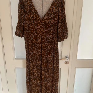 Brun leopardmönstrad långklänning ASOS - Snygg långklänning från ASOS DESIGN Curve med leopardmönster i brunt och svart. Klänningen har v-ringad hals, korta puffärmar och ett flowy fall. Perfekt för dig som gillar djurmönster och vill sticka ut med en cool look.