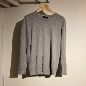 Grå tröja i pima bomull från Riley - En stilren grå tröja från Riley i mjuk pima bomull. Tröjan har rund halsringning, långa ärmar och en klassisk passform. Perfekt för lager-på-lager och funkar året runt. Enkel och clean look som passar till allt. Den är som ny använd 4 gånger! Hör av dig vid minsta fundering!