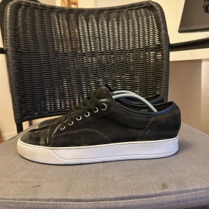 Lanvins - Snygga svarta sneakers från Lanvin med ovandel i mocka och tåparti i blankt skinn. Skorna har vita, platta sulor och klassisk snörning. Perfekta för dig som gillar stilrena och exklusiva sneakers med en lyxig touch.