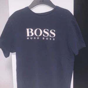Mörkblå Hugo Boss t-shirt - Snygg mörkblå t-shirt från Hugo Boss med stor vit logga på bröstet. Klassisk rund halsringning och korta ärmar. Perfekt för dig som gillar stilrena och trendiga plagg med premiumkänsla.