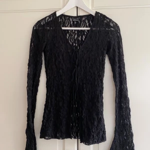 Svart spetsblus från Gina Tricot - Säljer en svart blus från Gina Tricot i storlek XS. Blusen är helt i spets med långa ärmar och v-ringad hals. Den har snörning framtill som ger en snygg detalj och är transparent. 