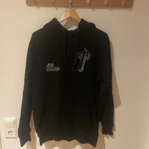 Svart Trapstar hoodie med tryck - Svart hoodie från Trapstar med vit grafisk text och tryck både fram och bak. Klassisk känguruficka, snörning i huvan och mjukt material. Snygg streetwear vibe och perfekt för dig som gillar unika detaljer.