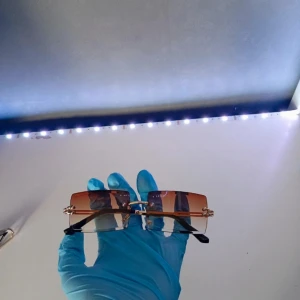 Solglasögon  - Rektangulära solglasögon 🕶️ med brun tonade linser och tunna guldfärgade skalmar. Tidlös design, stilren passform och exklusiv känsla  perfekta året runt.