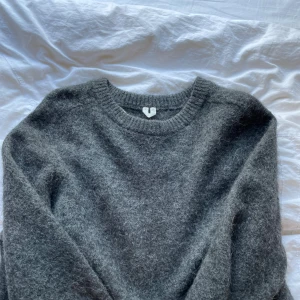 Grå stickad tröja i ull/mohair, storlek M - Mysig grå stickad tröja i ull med rund halsringning och långa ärmar. Tröjan har en klassisk passform och är perfekt för kyliga dagar. Den har en fluffig och mjuk känsla som gör den extra skön att bära. Gjord av Mohair, är från Arket.