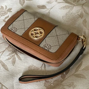 Beige och brun plånbok - Snygg plånbok i beige och brunt med klassiskt mönster och guldfärgad logga framtill. Plånboken har dragkedja runtom, flera fack för kort och mynt samt en praktisk handledsrem. Perfekt storlek för att ha med sig överallt. Denna är köpt för länge sen, men använts en gång! 🤎