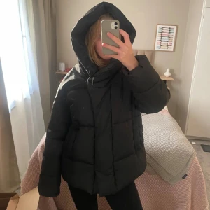 Svart pufferjacka med huva - Säljer min superfina hm vinterjacka som blivit väldigt populär!  Bra skick men skulle säga att den har tecken på användning :)  Storlek 34, beskriver den som oversized!  Supermysig luva och jättevarm! Den har knappar, inte dragkedja!