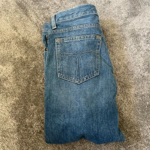 Blå jeans från Tiger of Sweden - Snygga blå jeans från Tiger of Sweden med klassisk femficksdesign och raka ben. Jeansen har orangea sömmar och en stilren look som funkar till det mesta. Modellen är straight och materialet är robust denim i bomull.