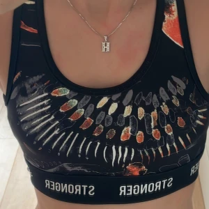 Svart sport-bh från Stronger XS - Sport-bh från Stronger i svart med färgstarkt grafiskt mönster i orange, vitt och grönt. Resår med logga runt om, brottarrygg och cool cutout-detalj bak. Perfekt för träning och ger en sportig vibe.Aldrig använd🥰Pris kan diskutera