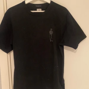 Svart t-shirt från C.P. Company - Svart t-shirt från C.P. Company med tryckt motiv av logga under. Tillverkad i 100% merceriserad bomull för en mjuk och lyxig känsla. Klassisk passform och rund halsringning och sjävklart 100% äkta då den är köpt på NK i Gbg 