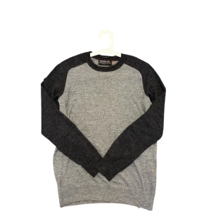 Grå långärmad tröja från Superdry - Snygg gråmelerad tröja från Superdry med mörkgrå ärmar och krage. Tröjan har rund halsringning och är tillverkad i mjuk bomull. Perfekt för dig som gillar en stilren och enkel look.