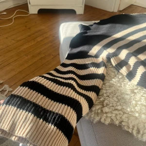Randig stickad tröja från Vila - Säljer en tröja från Vila i svart och beige med breda ränder. Tröjan har lång och utsvängd ärm, hög hals och är gjord i ett mjukt stickat material. Använd en gång, alltså i nytt skick!