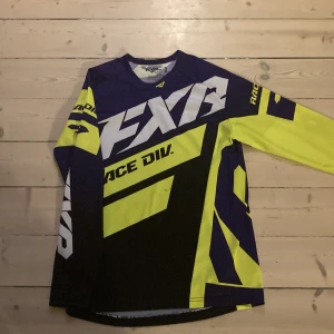 FXR långärmad tröja i neon och svart - Säljer en sportig långärmad tröja från FXR i svart, neon-gul och vit med stora tryck och grafiska detaljer. Tröjan är tillverkad i 100% polyester och har en loose passform, perfekt för dig som gillar att sticka ut med din stil.