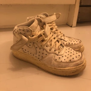 Nike Air Force 1 vita med stjärnor - Unika Nike Air Force 1 sneakers i vitt med coolt stjärnmönster över hela skon. Modellen är high-top med snörning och kardborreband upptill. Skorna har en klassisk rund tå och platt sula. Storlek 38,5