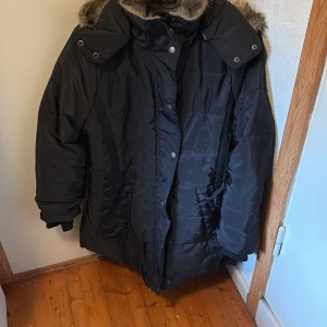 Svart pufferjacka med fuskpäls - Säljer en svart pufferjacka med huva och fuskpäls. Avtagbar luva och en dragkedja på huvan. Använda fåtal gånger. Perfekt för höstiga dagar. Den är en M men skulle mer säga den passar en s