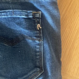 Blå bootcut jeans från Replay - Säljer ett par snygga blå jeans från Replay med klassisk femficksdesign och bootcut-ben. Jeansen har en mörkblå tvätt, kontrastsömmar och Replay-logga på bakfickan. Tillverkade i mjukt jeanstyg som sitter skönt hela dagen. Strl. 25/34