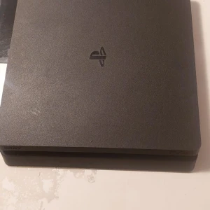 PlayStation 4 Slim - Sony PlayStation 4  i fint skick, komplett med strömkabel, HDMI och USB-kabel. Två handkontroller (svart och röd) samt tre populära spel: FIFA 21, NBA 2K24 och EA FC24 ingår. Konsolen har mindre yttre slitage men fungerar utmärkt.