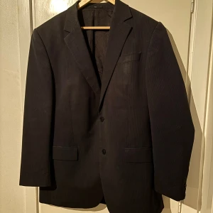 Svart kavaj - Stilren svart kavaj med diskreta prickar och klassisk passform. Två knappar framtill, fickor med lock och bröstficka. Perfekt för dig som vill ha en tidlös och snygg look.