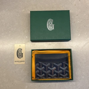  blå plånbok med mönster - Snygg plånbok  i marinblått med det klassiska mönstret i vitt och brunt. Plånboken är tillverkad i skinn och har flera fack för kort. Kommer i original grön ask med gul insida och  Paris-tag.