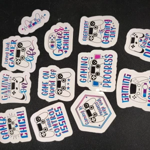 Gaming Stickers Set - Färgglada stickers med gamingtema, motiv av spelkontroller och roliga texter som 'Gamer Chick', 'Gaming Progress' och 'Game On'. Perfekt för att dekorera laptops, konsoler eller tillbehör. Alla stickers är i nyskick utan synligt slitage.