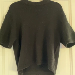 Svart stickad t-shirt från Gina Tricot - Mysig svart stickad tröja från Gina Tricot i ullblandning. Tröjan har korta ärmar och en avslappnad passform med rund halsringning. Perfekt att styla med jeans eller kjol för en enkel och snygg look. PRIS KAN DISKUTERAS 