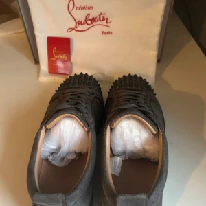 Grå mocka sneakers från Louboutin - Säljer ett par grå sneakers från Christian Louboutin i mocka med coola nitar på tån. Skorna har snörning och en platt sula, perfekt för dig som vill sticka ut med en edgy vibe. Klassisk rund tå och exklusiv känsla, passar till allt från jeans till dressade outfits.