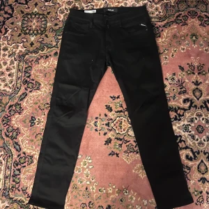 Svarta Replay Anbass Hyperflex jeans 32/30 - Svarta Replay Anbass Hyperflex jeans med klassisk femficksdesign och diskreta sömmar. Byxorna har slim passform och är tillverkade i stretchigt jeansmaterial för extra komfort. Märkesdetaljer på ficka och bakre läderpatch. Perfekta för en clean och stilren look. Midja 41cm längd 100cm (47)