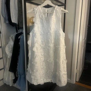 Vit blommig kort klänning - Superfin vit ärmlös klänning med 3D-blommor och broderade detaljer. Kort modell med rund halsringning och dragkedja bak. Perfekt för sommarens alla tillfällen när du vill sticka ut lite extra. Sitter som en M