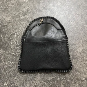 Svart plånbok i skinn med dragkedja - Svart plånbok i skinn med snygg kantdetalj och metallspänne framtill. Plånboken har två dragkedjefack och magnetknapp för smidig stängning. Perfekt storlek för kort och smågrejer, stilren och enkel att ta med sig.