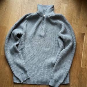 Grå stickad half zip från Jack & Jones - Säljer en grå stickad tröja från Jack & Jones med hög krage och half zip-dragkedja. Tröjan har lång ärm, ribbade muddar och är i grovstickad bomull. Perfekt för lager-på-lager under kyliga dagar.