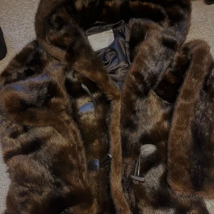 Mörkbrun pälsjacka från Zara Woman - Säljer en fluffig och lyxig mörkbrun pälsjacka från Zara Woman. Jackan har huva, stora knappar i hornstil och är helfodrad med glansigt tyg. Perfekt för dig som vill sticka ut och hålla dig varm under kalla dagar.