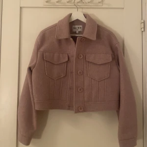 Ljusrosa/Lila Jacka från NAKD - Hej! Jag Säljer en ljusrosa/ Lila jacka från NA-KD med croppad passform, aldrig använd, stora bröstfickor och knappar framtill. Jackan har en klassisk krage och är Perfekt för lager-på-lager och snygg till både jeans och kjol.