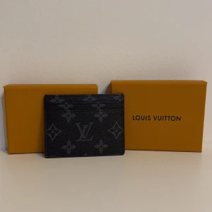 L och V svart korthållare - Snygg svart korthållare från L och V med klassiskt monogrammönster i grått. Tillverkad i exklusivt skinn med plats för flera kort. Perfekt accessoar för dig som vill ha stil och funktion i ett smidigt format.