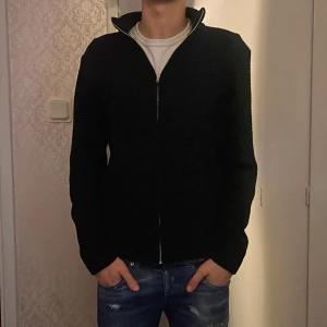 Stickad kofta! - Svart stickad kofta med hel dragkedja framtill och hög krage. Tröjan har en clean och stilren look, perfekt till jeans eller chinos. Långärmad modell med normal passform och mjukt material som känns skönt mot huden.