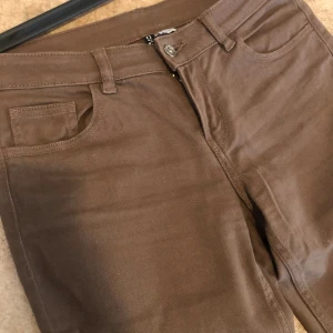 Bruna bootcut byxor i bomull - Snygga bruna byxor med bootcut-modell och klassisk femficksdesign. Tillverkade i mjuk bomull med dragkedja och knapp framtill. Perfekta för dig som gillar en stilren och enkel look med lite utsvängda ben.