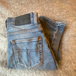 Tiger of sweden jeans - Säljer ett par klassiska blå skinny jeans med svarta detaljer vid linningen. Jeansen har fem fickor, smal passform och är tillverkade i stretchigt denimtyg för en bekväm känsla. Perfekta för dig som gillar en tajt look och vill ha ett par stilrena jeans i garderoben.
