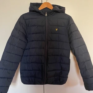 Mörkblå pufferjacka från Lyle & Scott - Riktigt snygg och bekväm mörkblå pufferjacket från Lyle & Scott, jackan passar perfekt för höst och vinter! Den håller dig varm utan att kännas tung, tack vare det lätta och smidiga materialet. Storleken är 14/15 år ≈ XS. Pris går att diskutera.  ✔️ Varm och skön – perfekt för kallare dagar ✔️ Lättviktsdesign som gör den bekväm att bära ✔️ Klassisk passform och snygg quiltad stil ✔️ Mycket bra skick – inga synliga tecken av användning 