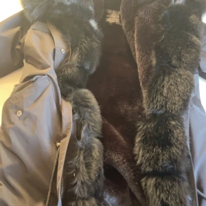 Svart parkajacka med päls överallt i insidan - Säljer en svart parkajacka från Interessing i storlek S. Jackan har mjukt fuskpälsfoder och stora fuskpälsdetaljer längs huva och öppning. Yttermaterialet är tåligt och jackan har dragkedja och tryckknappar. Perfekt för kalla dagar och riktigt snygg stil.