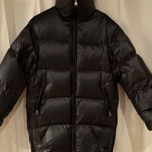 Svart pufferjacka från Arket stolek: XS  - Säljer en svart pufferjacka från Arket med hög krage och dragkedja framtill. Jackan är fylld med återvunnen dun (Re:Down) och har två fickor med dragkedja. Perfekt för kalla dagar och riktigt skön att bära. Håller värmen bra. 