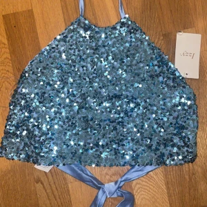 ONESIZE blå festtopp med sidenband - Säljer en glittrig topp med paljetter. Toppen knyts i nacke och rygg, så storleken kan justeras. Passar XS, S, M, L  beroende på hur man knyter det. Perfekt till fest, nyår eller en utekväll. Helt nytt, aldrig använt och med tag kvar. 