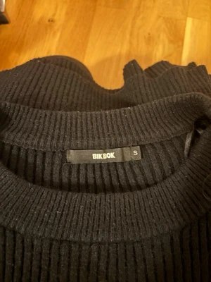 Svart ribbad stickad tröja BikBok - Säljer en svart ribbad stickad tröja från BikBok i storlek S. Tröjan har en croppad passform, rund halsringning och långa ärmar. Perfekt till höst och vinter för en chill och enkel look.