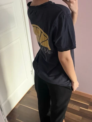 Svart Acqua Limone t-shirt med citrontryck - Svart t-shirt från Acqua Limone med klassiskt citrontyck i gult på ryggen och logga framtill. T-shirten har korta ärmar, rund hals och en liten ficka nedtill på baksidan. Tillverkad i mjuk bomull och har en relaxed, loose fit.