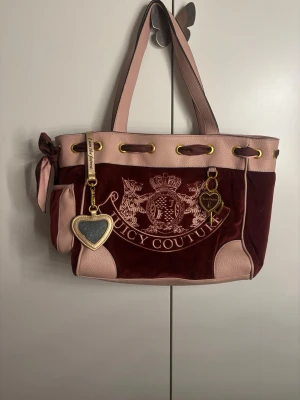 Juicy Couture vinröd axelväska - Juicy Couture axelväska i vinröd sammet med ljusrosa skinn-detaljer och guldfärgade metalldelar. Praktiska fack och breda axelband. Priset kan diskuteras. ❤️