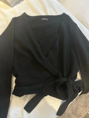 Svart omlottkofta från Even&Odd - Säljer en svart omlottkofta från Even&Odd med knyt i midjan. Koftan har lång ärm och djup v-ringning, perfekt att styla med ett linne eller topp under. Mjuk och skön stickad känsla som passar till många olika looks.