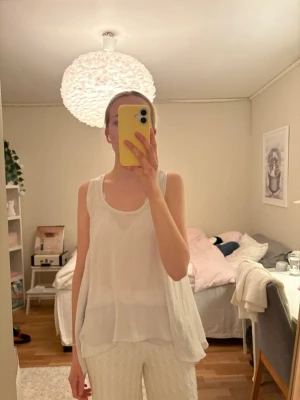 Vit flowy linnetopp från KappAhl - Säljer en superfin vit ärmlös linnetopp från MassimoDutti. Toppen är flowy och luftig med dubbla lager och en snygg detalj baktill. Perfekt för varma dagar och enkel att styla med både jeans och kjol.