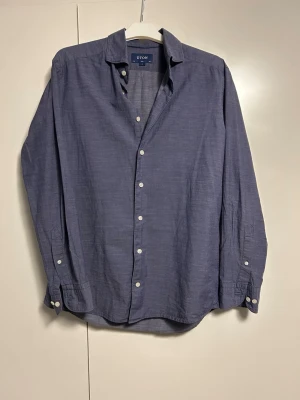 Blå slim fit skjorta från Eton - Snygg blå skjorta från Eton i slim fit-modell. Skjortan har klassisk krage, vita knappar och är långärmad. Tillverkad i ett lätt och luftigt material som passar perfekt till både jeans och chinos.