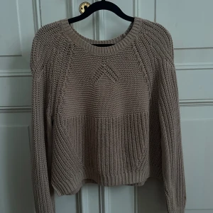 Beige/brun stickad tröja - Stickad tröja i en varm beige/brun nyans med fin strukturstickning och rund hals.  Tröjan är i fint använt skick med normal användningskänsla, däremot finns de en liten fläck på ärmen( kan skicka bild)